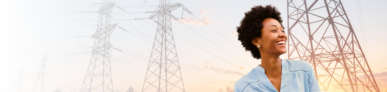 A person standing outdoors near large electrical transmission towers at sunset, with power lines stretching across the sky.