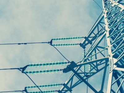 Close-up of a high-voltage transmission tower with metal lattice structure and electrical cables attached to green insulators against a partly cloudy sky.