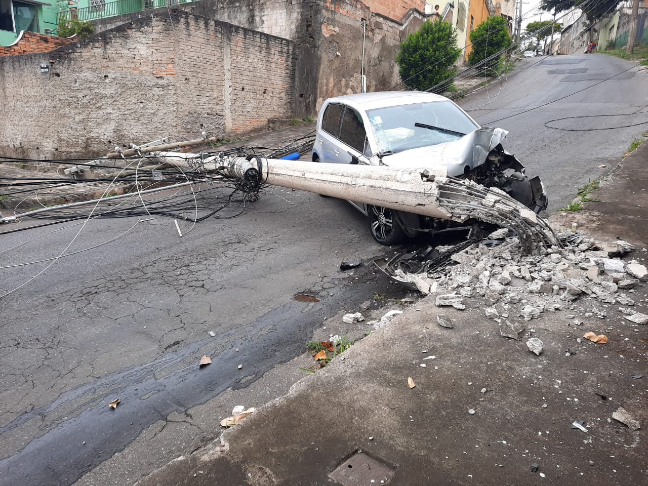 Imagem de um carro acidentado em frente a um poste caído