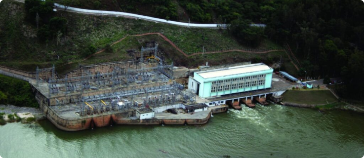 Vista aérea de uma estrutura hidrelétrica com reservatório e área de subestação elétrica.