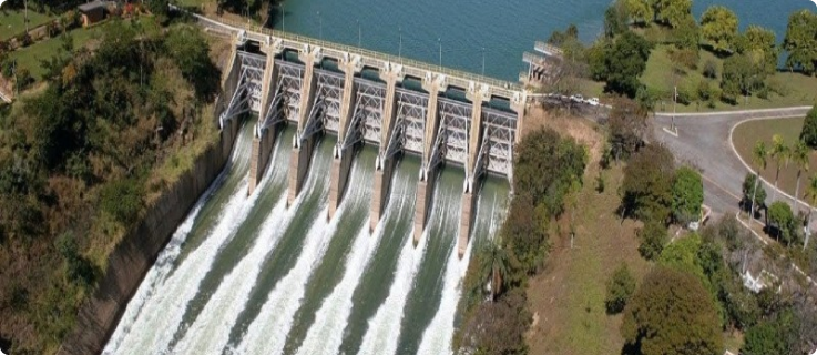 Imagem aérea da usina hidrelétrica de Três Marias com múltiplos vertedouros liberando água.