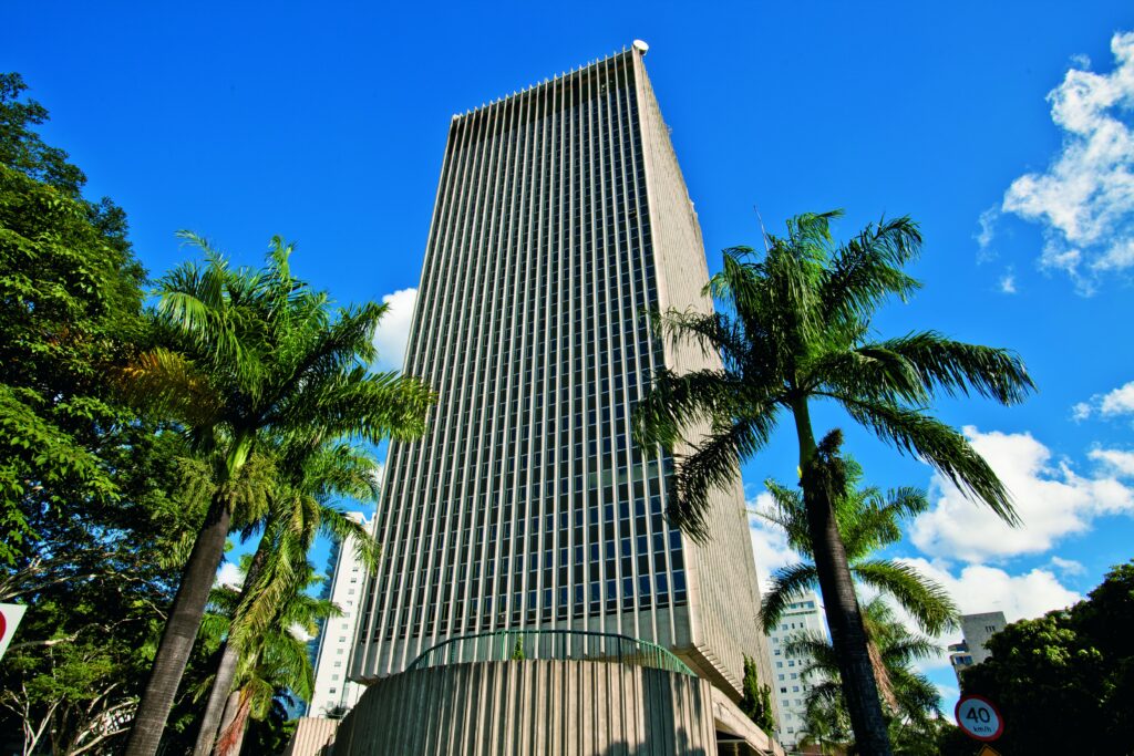 Foto com o edifício sede da Cemig ao fundo e palmeiras nas laterais.