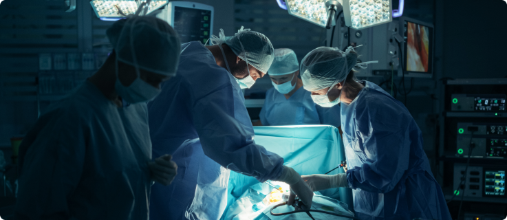 Equipe médica realizando cirurgia em uma sala de operação com iluminação intensa e equipamentos hospitalares ao fundo.