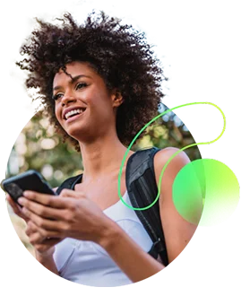 Uma mulher de cabelos cacheados sorrindo, segurando um smartphone e com uma mochila nas costas. Ela parece estar em um ambiente ao ar livre.