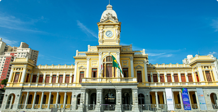 Fachada do Museu de Artes e Ofícios em Belo Horizonte durante o dia, com céu azul ao fundo e bandeira do Brasil ao centro.
