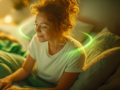 Uma jovem ruiva sorrindo enquanto usa um notebook na cama, com um anel de luz verde neon brilhante circulando ao redor de seus ombros em um quarto com iluminação quente e aconchegante.