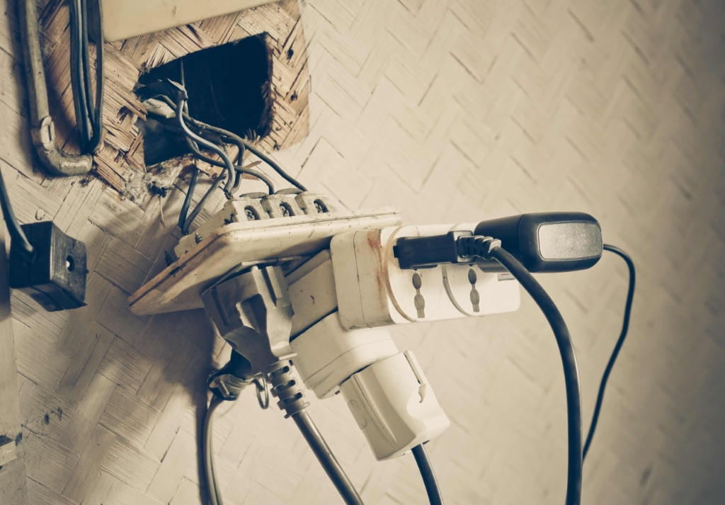 imagem de uma tomada mal-conservada, com vários aparelhos ligados. 