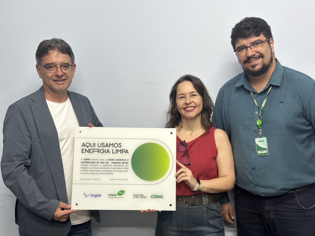 A imagem mostra três pessoas em pé, lado a lado, diante de uma parede clara. Elas seguram um placa retangular que celebra o uso de energia limpa.

Na placa, em destaque, está escrito:
“AQUI USAMOS ENERGIA LIMPA”.

O texto explica que a Cemig fornece energia renovável e certificada para a empresa Logás Logística e Distribuição de Gás S/A – Unidade Betim, em conformidade com os Objetivos de Desenvolvimento Sustentável da ONU, relacionados à produção de energia limpa e preservação ambiental.

A placa também traz a data e período de validade: Belo Horizonte – Janeiro/2023 | Período: 02/2023 a 01/2024.
Na parte inferior aparecem os logotipos da Logás, da Cemig e do programa Energia Livre Cemig.

Em resumo, a cena transmite uma mensagem de sustentabilidade e responsabilidade ambiental, destacando o reconhecimento oficial de que a unidade utiliza energia renovável.
