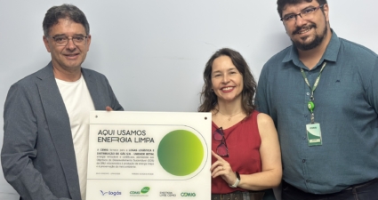 A imagem mostra três pessoas em pé, lado a lado, diante de uma parede clara. Elas seguram um placa retangular que celebra o uso de energia limpa. Na placa, em destaque, está escrito: “AQUI USAMOS ENERGIA LIMPA”. O texto explica que a Cemig fornece energia renovável e certificada para a empresa Logás Logística e Distribuição de Gás S/A – Unidade Betim, em conformidade com os Objetivos de Desenvolvimento Sustentável da ONU, relacionados à produção de energia limpa e preservação ambiental. A placa também traz a data e período de validade: Belo Horizonte – Janeiro/2023 | Período: 02/2023 a 01/2024. Na parte inferior aparecem os logotipos da Logás, da Cemig e do programa Energia Livre Cemig. Em resumo, a cena transmite uma mensagem de sustentabilidade e responsabilidade ambiental, destacando o reconhecimento oficial de que a unidade utiliza energia renovável.